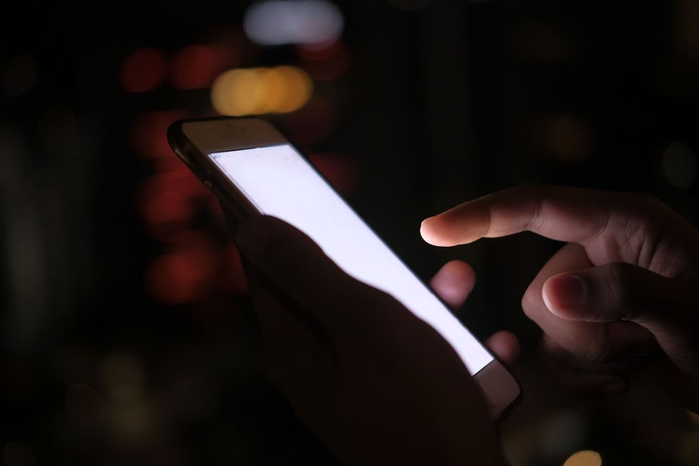 Des mains tenant un téléphone allumé dans l'obscurité